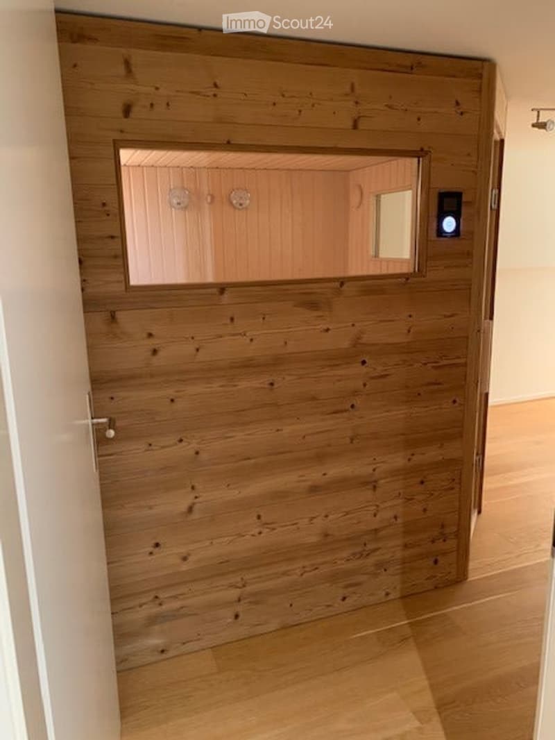 A wooden door with a frosted glass panel is visible, leading to a room with wooden walls and a mirror. The hallway has light wooden flooring and white walls.
