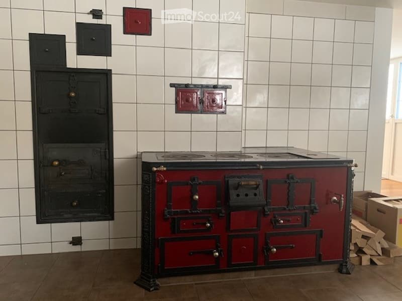 Vintage kitchen with a red and black stove and oven, white tiled walls, and wooden floor.