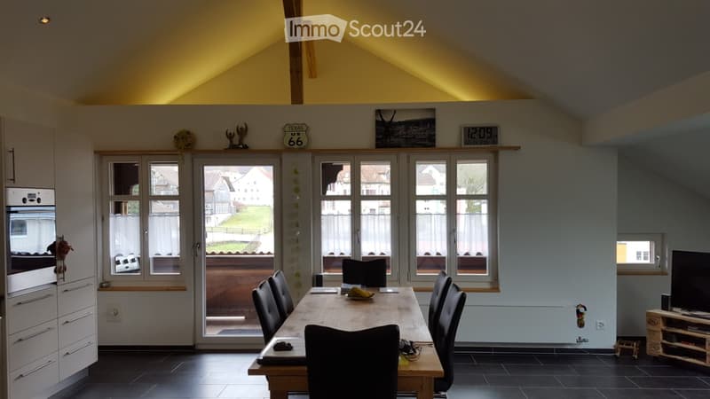 Bright, open room with a dining table and chairs, modern kitchen cabinetry, and large windows overlooking a yard.