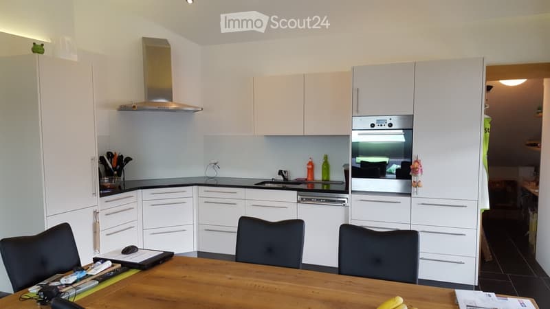 Modern kitchen with white cabinets, stainless steel appliances, a wooden dining table with chairs, and a laptop on the table.