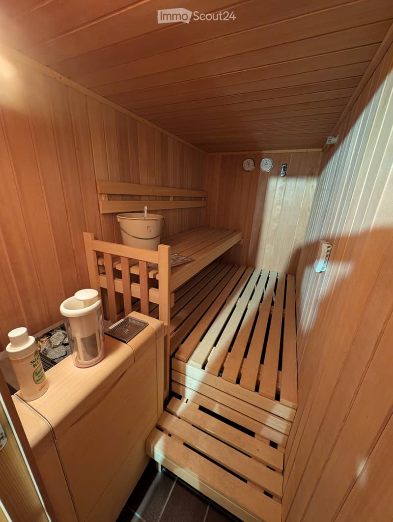Wooden sauna with benches, a bucket, and a bottle on a wooden shelf.