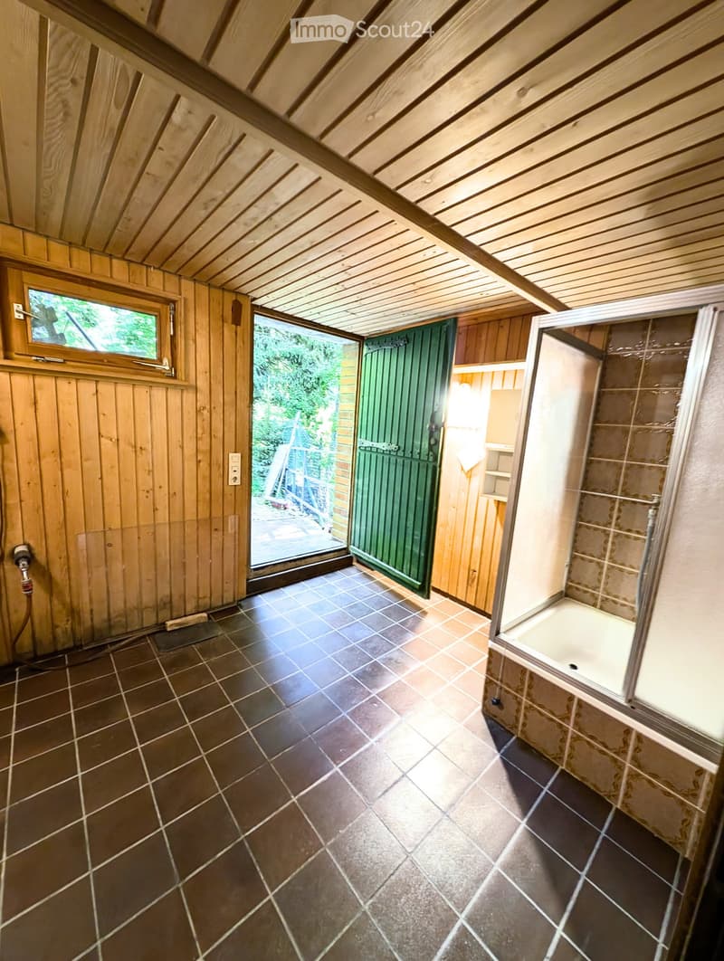 Bathroom with dark tiled floor, wooden walls, and a glass-enclosed shower stall. A green door leads outside.