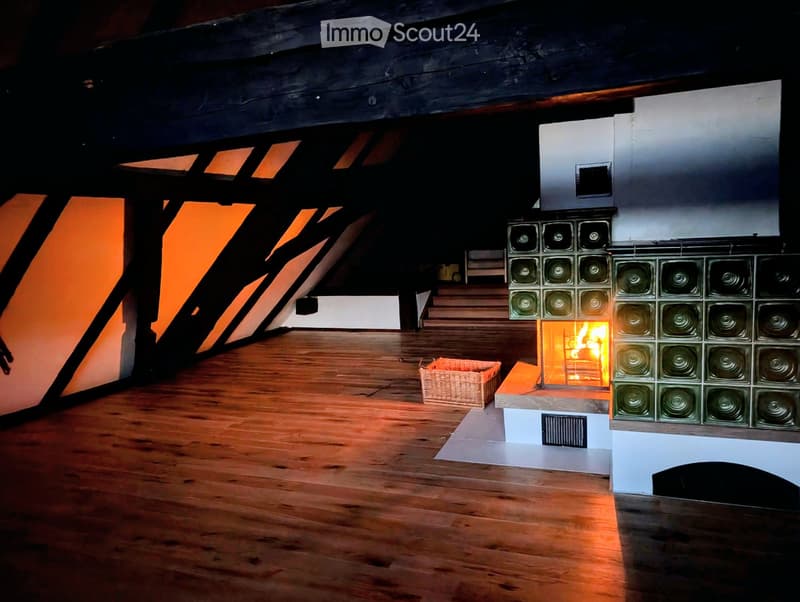Modern living room with exposed wooden beams, a central fireplace with glass tiles, and a wicker basket on the floor.