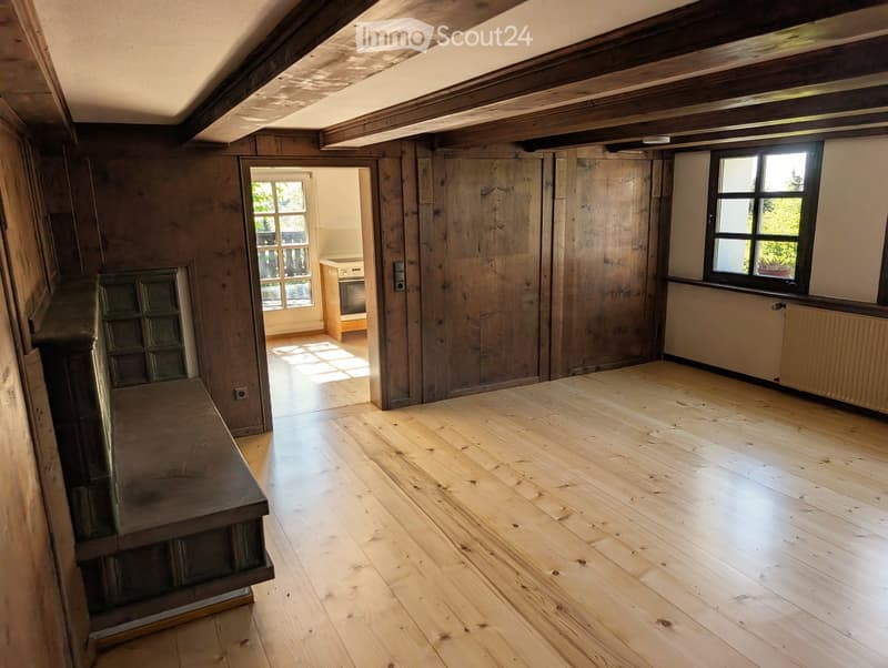 Empty room with wooden floors and exposed wooden beams on the ceiling. There are windows and a doorway leading to another room.