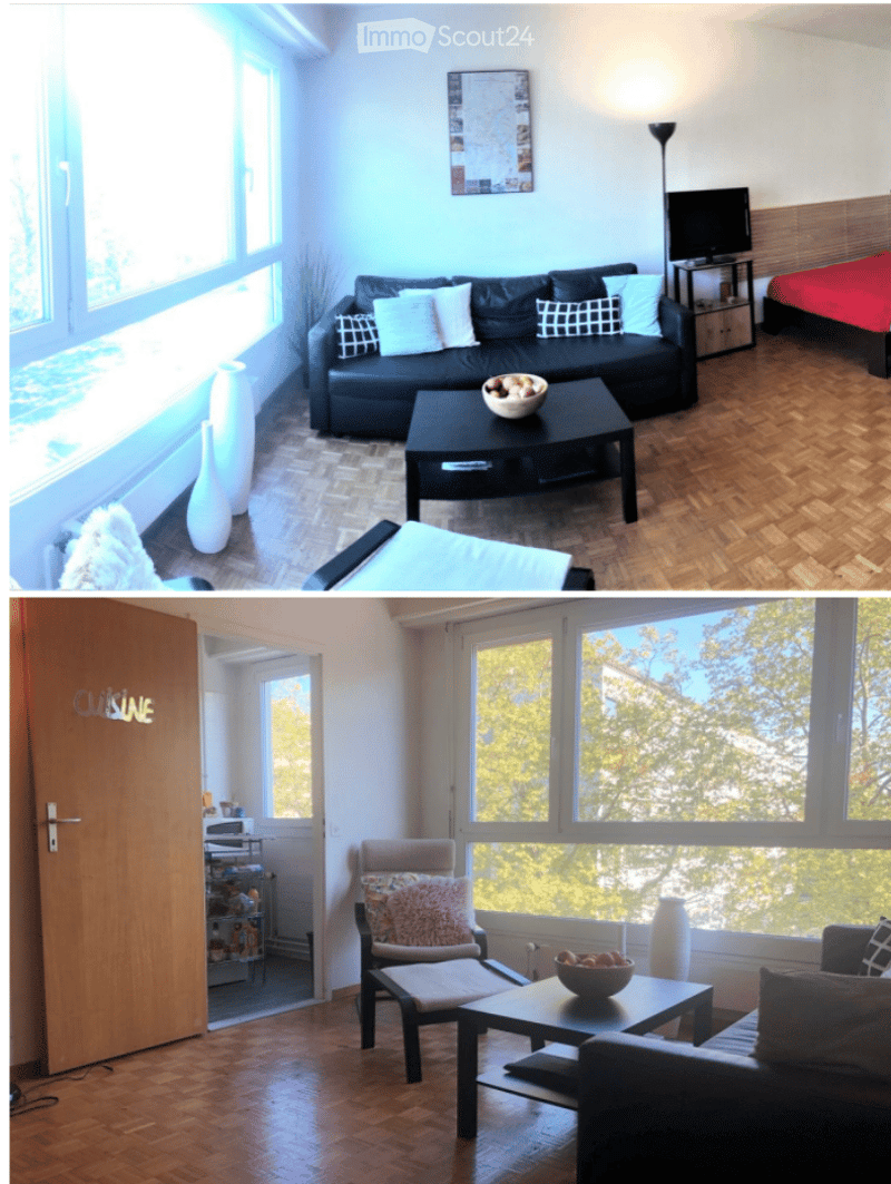 The image shows a modern, well-lit living space with a black leather sofa, a coffee table, a TV stand, a bed with red bedding, and decorative vases. The room features large windows with a view, wooden flooring, and a cozy seating area with a chair and sma