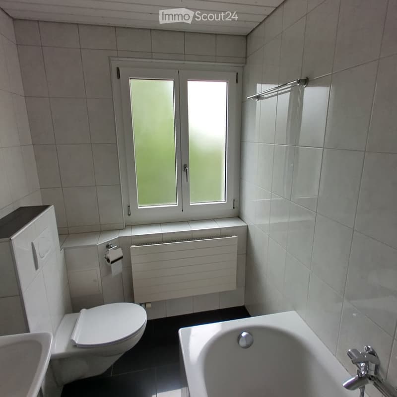 a small bathroom with white ceramic tiles, a toilet, a bathtub, and a radiator