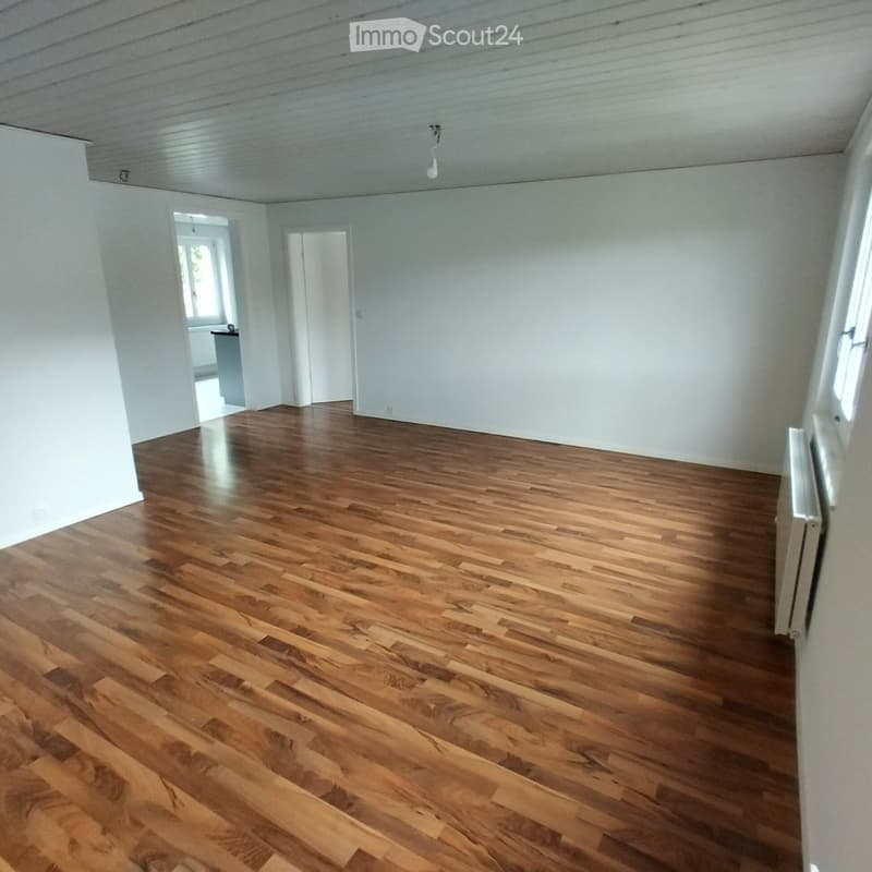 Empty room with wooden flooring, white walls, and a visible doorway leading to another room.