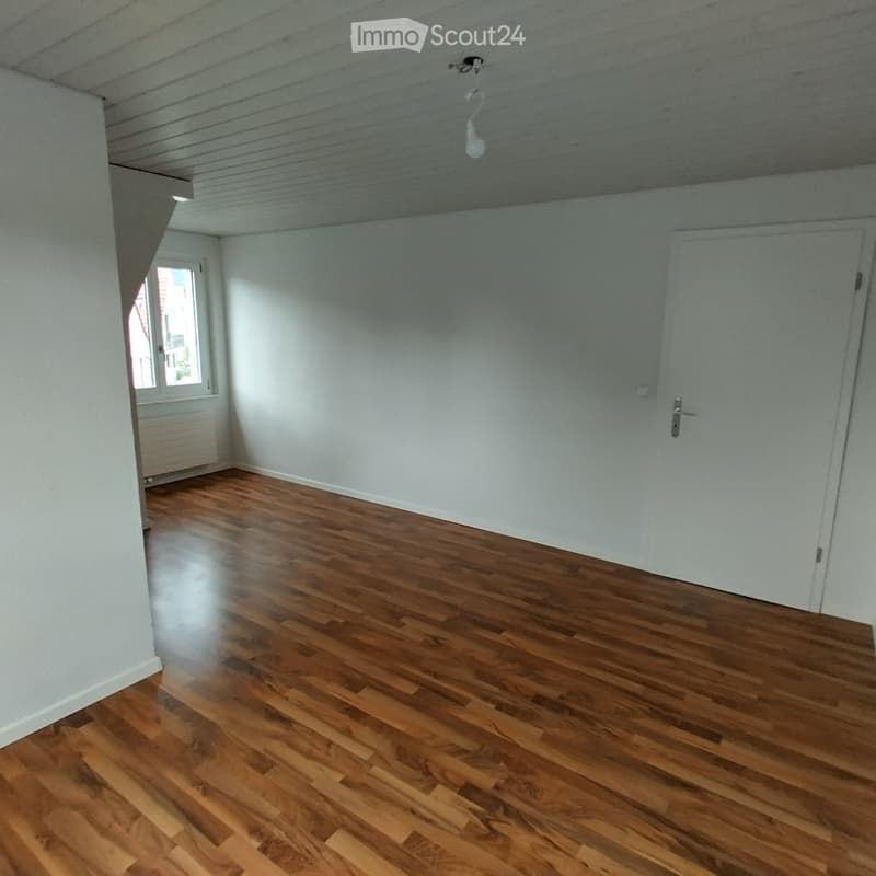 Empty room with wooden flooring, white walls, and a single door. Natural light enters through a window on the left side.