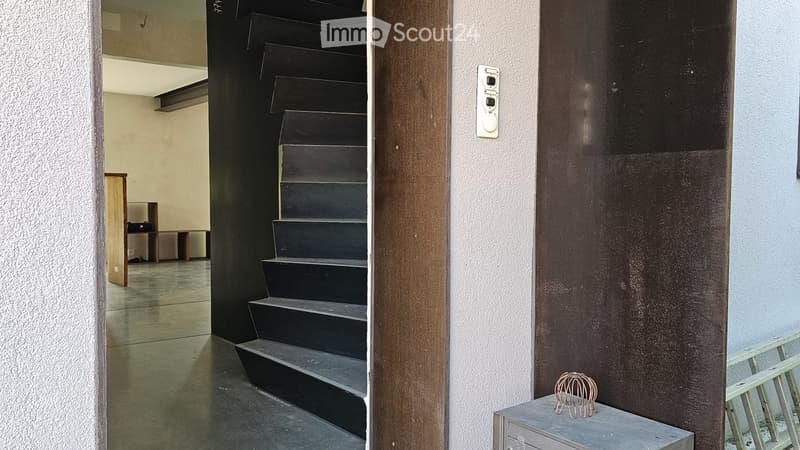 A modern hallway with a black staircase leading upwards, featuring a wooden door frame and a small decorative item on a table to the right.