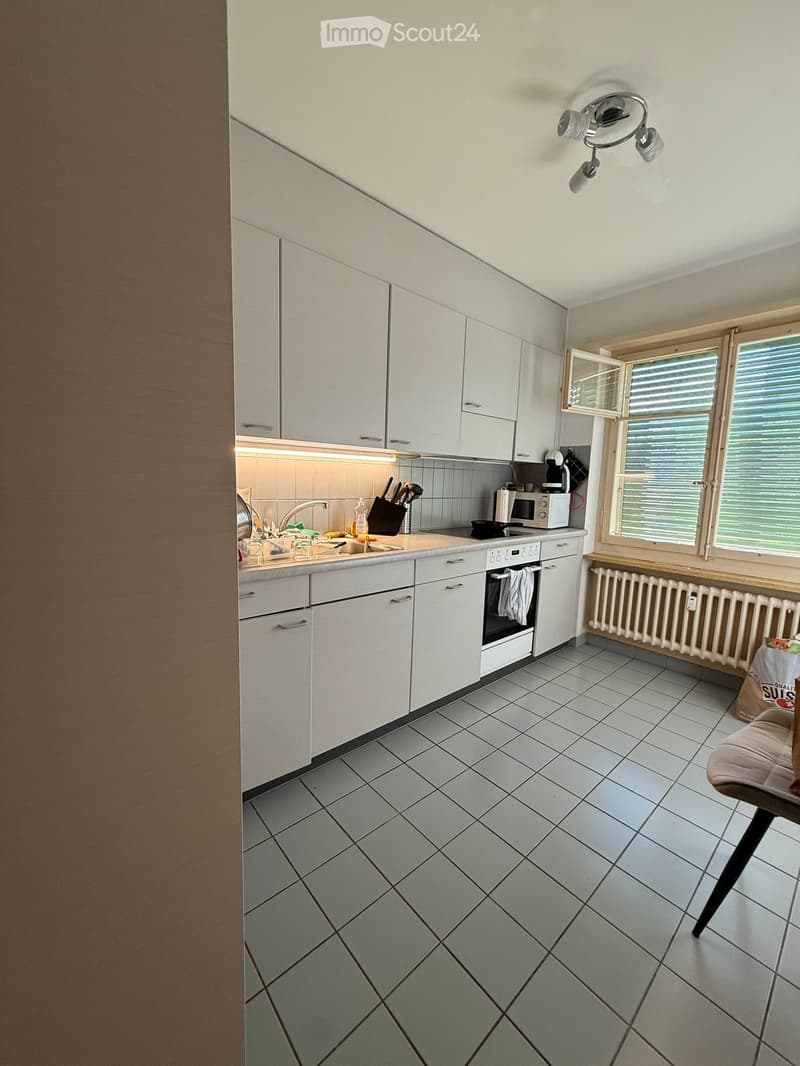 Modern kitchen with white cabinets, tiled floor, and stainless steel appliances. Features a sink, microwave, and knife block on the counter.