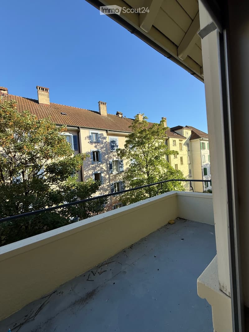 Balcony with a metal railing, overlooking a street with buildings and trees.