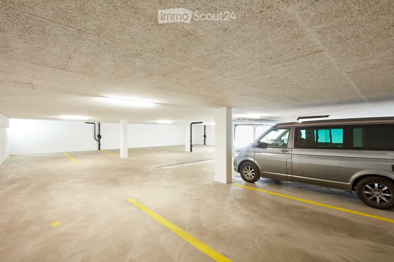Underground parking area with a single van parked inside, marked parking spaces, and white walls.