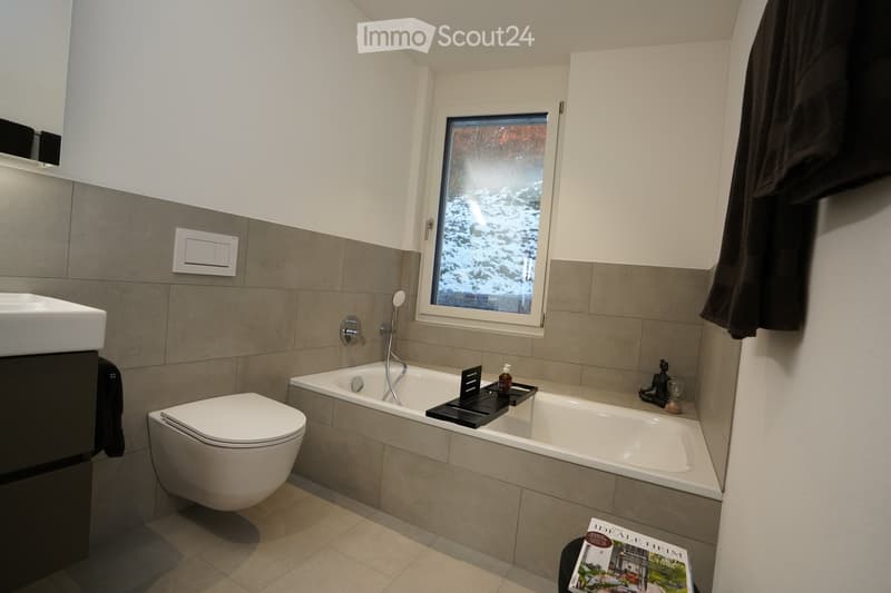 Modern bathroom with a large window showing a snowy outdoor view, featuring a sink, toilet, bathtub, and a towel hanging on the side.