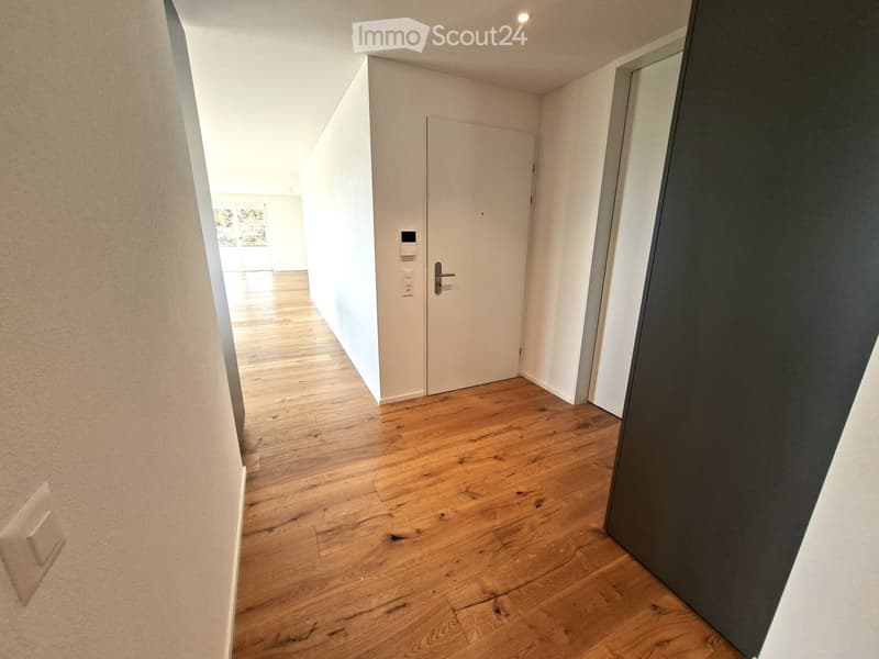 Empty hallway with wooden flooring, white walls, and a closed door leading to another room.