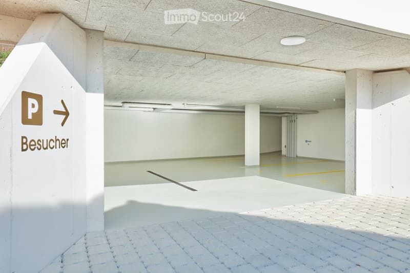Underground parking area with concrete pillars, white walls, and a sign indicating visitor parking.