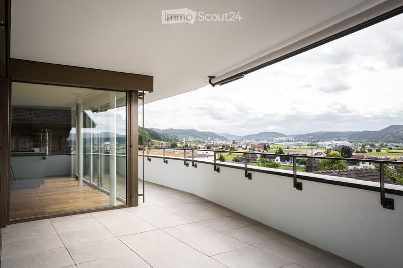 Modern balcony with tiled floor, glass sliding doors, metal railing, and scenic countryside view.