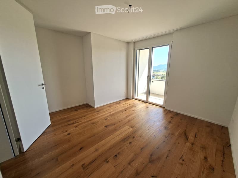 Empty room with wooden flooring, white walls, and a large sliding glass door leading to a balcony.