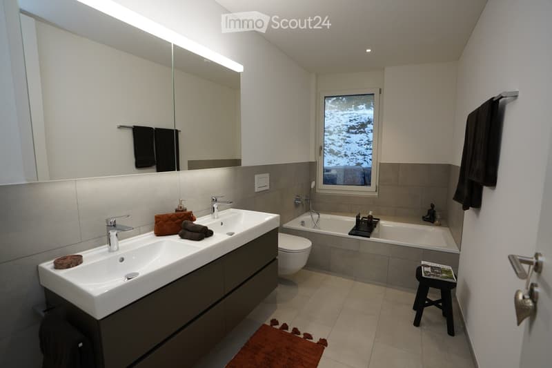 Modern bathroom with double sink, bathtub, toilet, large mirror, and window view of snowy landscape.