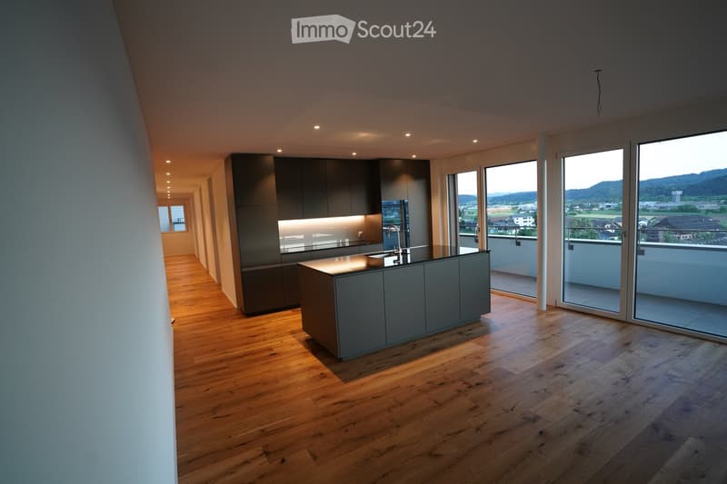 Modern kitchen with wooden flooring, grey cabinets, and a central island, featuring large windows offering a scenic view of the landscape.