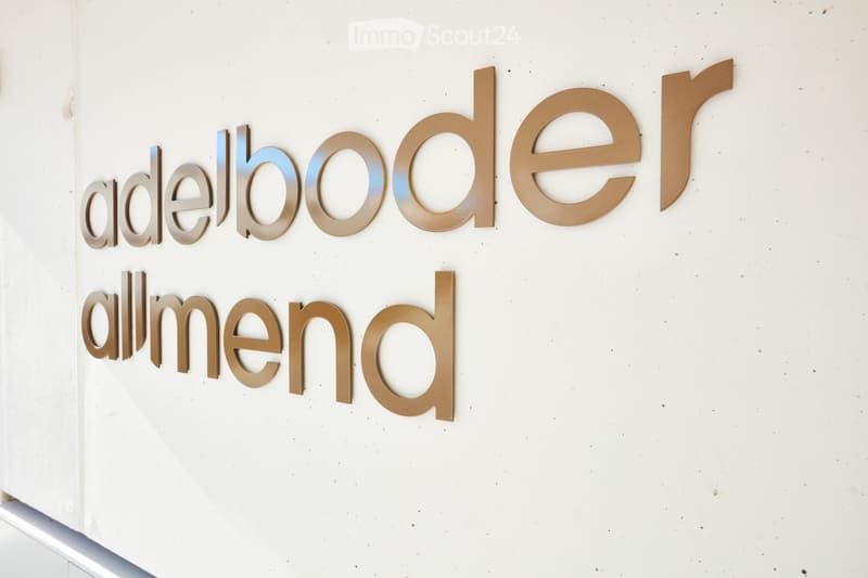 A white wall with large, three-dimensional metallic letters spelling out "adelboode" and "almennd" in a modern, sleek design.