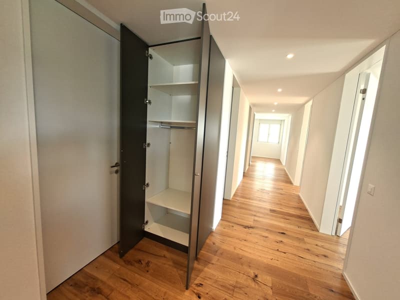 Empty hallway with wooden flooring, white walls, and a built-in closet with shelves and a hanging rod.