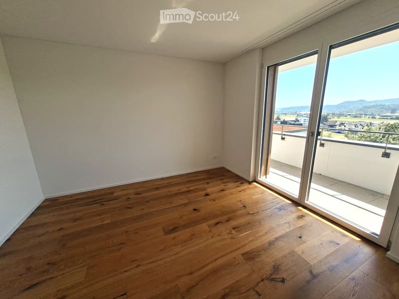 Empty room with wooden flooring and large sliding glass doors leading to a balcony with a scenic view.