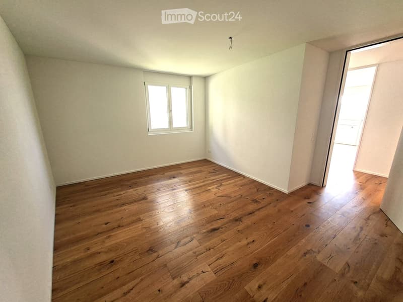 Empty room with wooden flooring, white walls, and a window with double panes. The room has a door leading to another space.