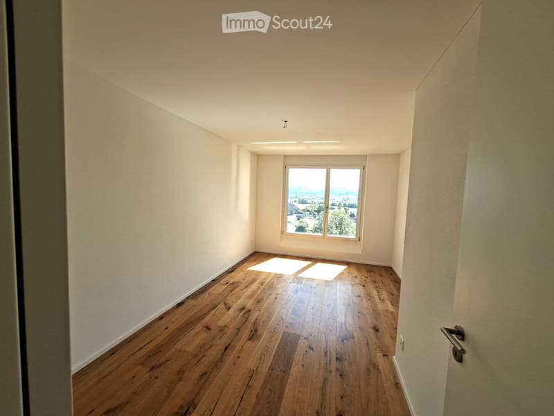 Empty room with wooden flooring, white walls, and a large window offering a scenic view.