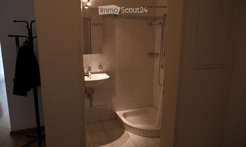 A small bathroom with a white sink, a bathtub, a mirror, and a towel rack. The walls are tiled, and the floor is tiled as well.