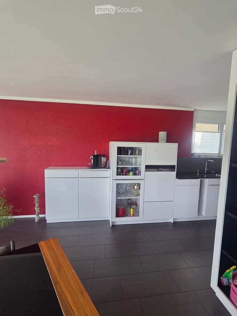 Modern kitchen with white cabinets, a coffee maker on the counter, and a display cabinet with glassware and cups. The walls are painted in a two-tone design with red lower half and white upper half.