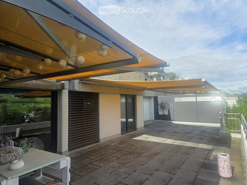 Covered outdoor patio with tiled floor, white table, decorative items, and scenic view of greenery.