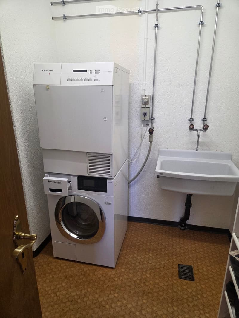 Bathroom with a washing machine and a sink, featuring a tiled floor and white walls.