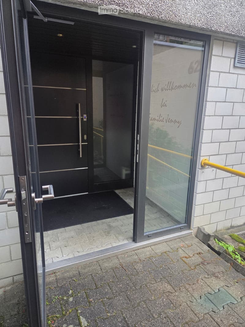 Entrance to a building with a black door and glass panel, featuring a welcome sign in German.