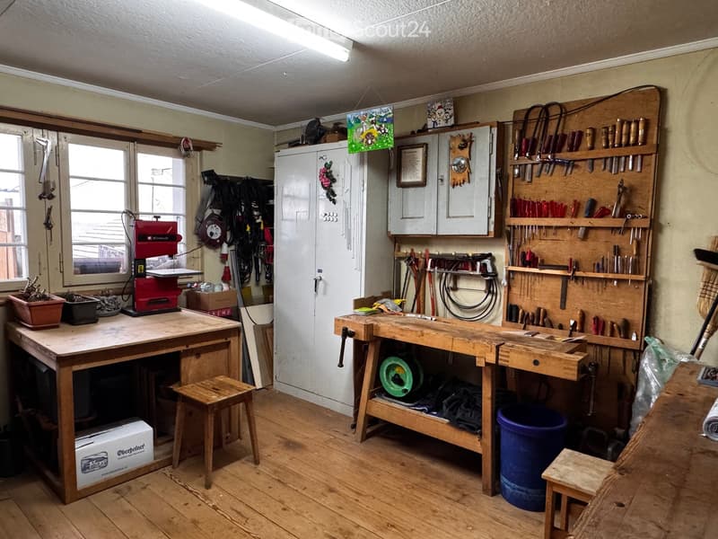 Well-organized workshop with wooden workbenches, tools, cabinets, and a saw on the table.