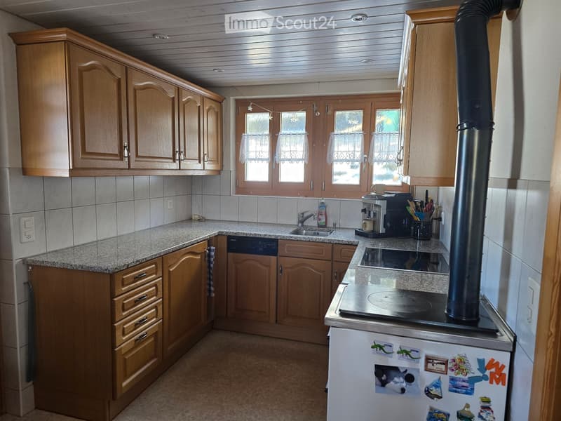 A well-lit kitchen with wooden cabinets, granite countertops, and various appliances including a coffee maker, refrigerator, and stove.