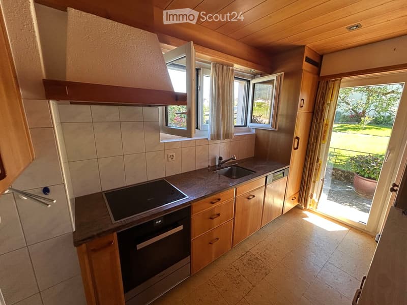 Modern kitchen with wooden cabinets, stainless steel appliances, and a large window overlooking a garden.