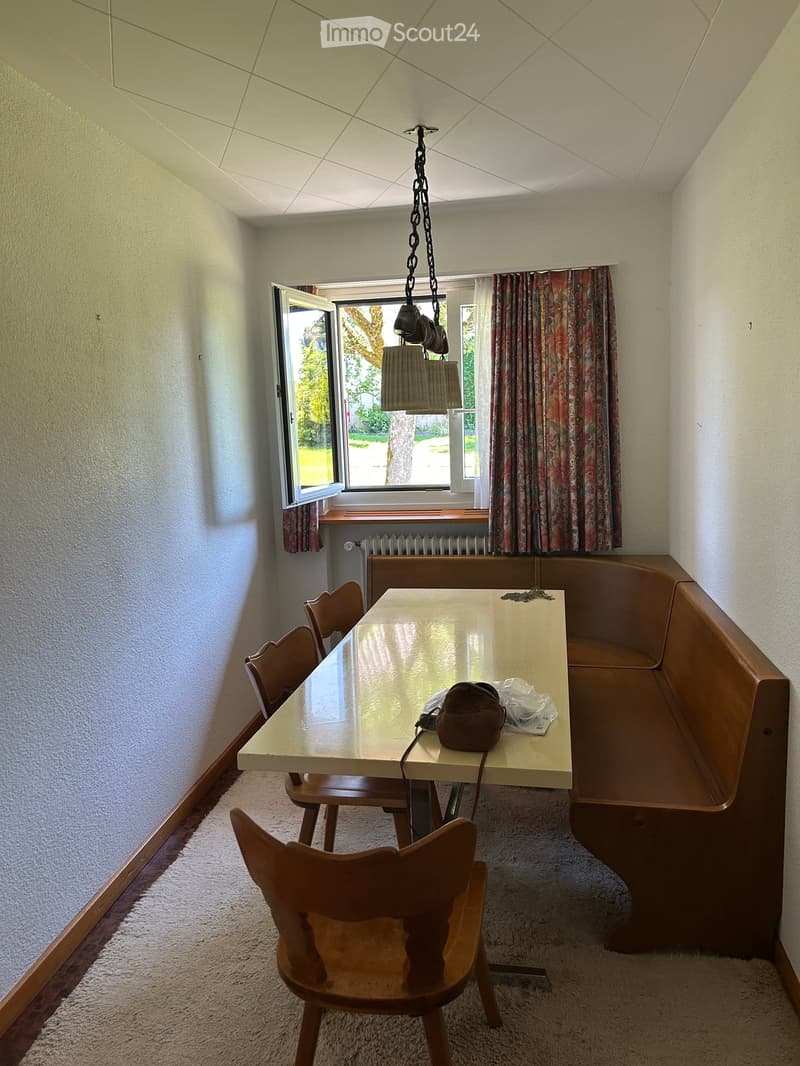 Dining area with a table, chairs, and a built-in bench, featuring a window with curtains and a hanging light fixture.