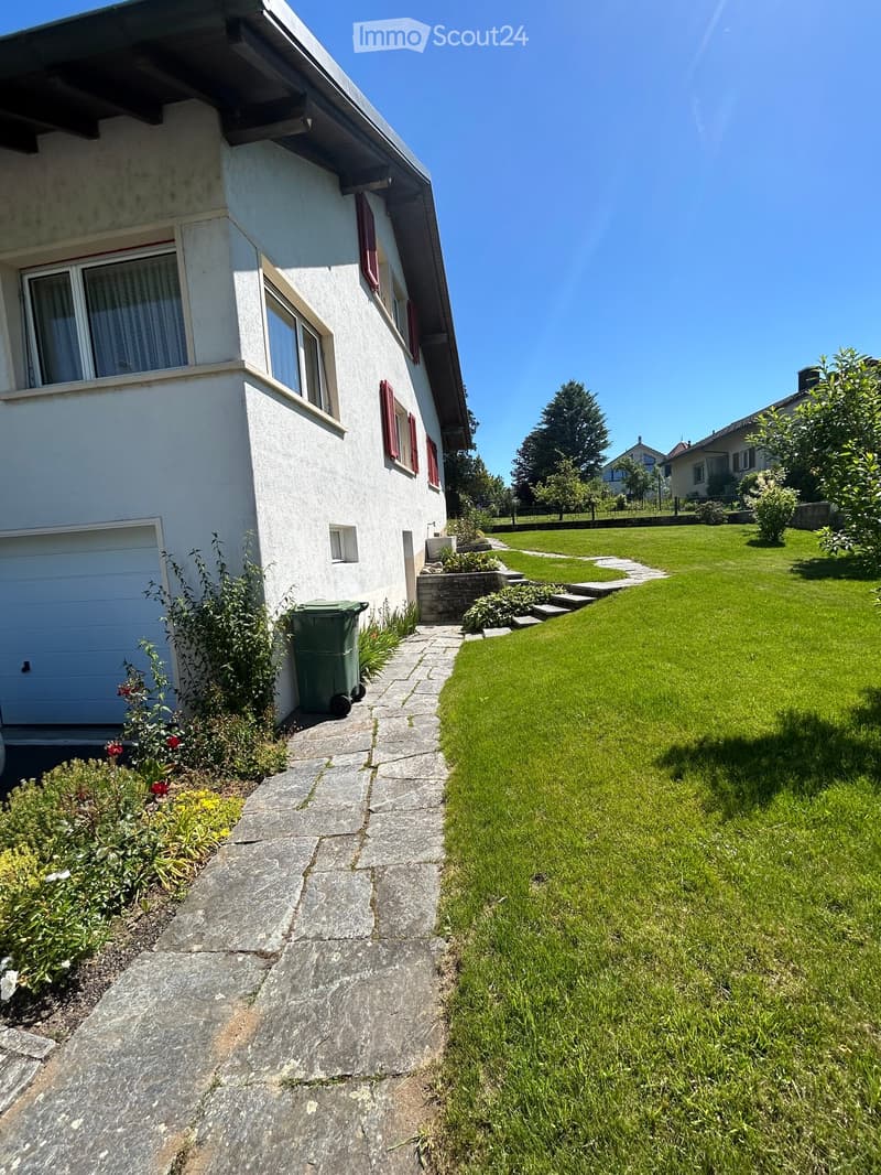 Two-story house with white exterior, red shutters, garage, and well-maintained garden with a stone pathway.