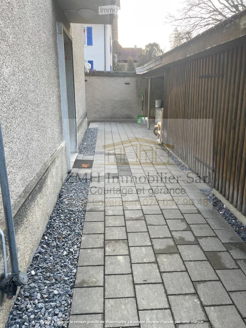 brick walkway leading to a building entrance with an open space behind it, paved with tiles