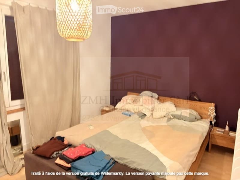 A room with a bed, pillows, two nightstands, night lamps, a lamp on the ceiling, and a couch with clothes