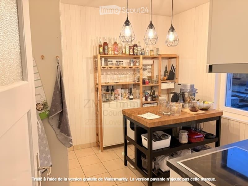 Open kitchen with wooden counter, shelves filled with bottles and kitchenware, kitchen tools, kettle, and kitchen island.