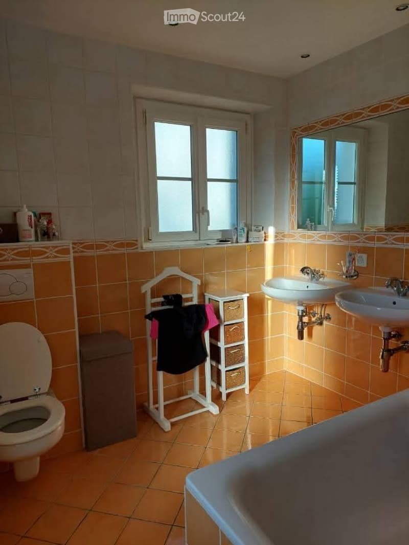 Bathroom with orange tiles, two sinks, a toilet, a bath, a coat rack, and a small storage unit.