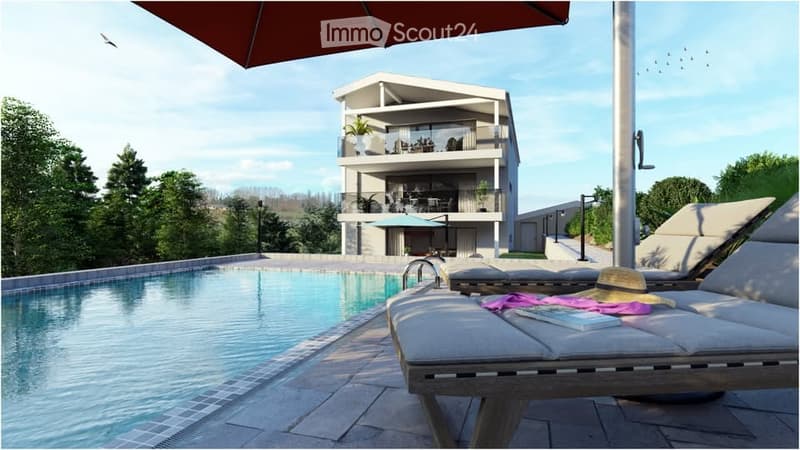 A modern two-story house with balconies and a swimming pool in the foreground. Outdoor furniture, including lounge chairs and a sun umbrella, is visible near the pool.