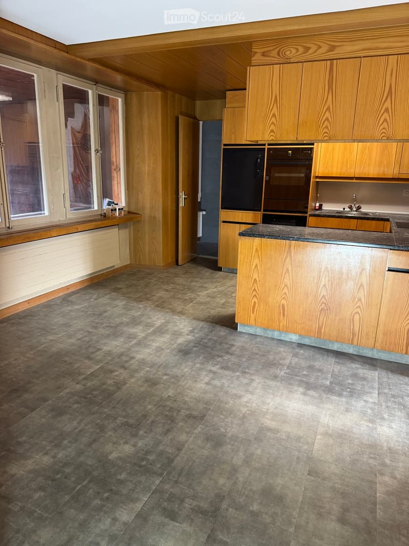 Empty kitchen with wooden cabinets, granite countertop, and tiled floor. No appliances or furniture present.