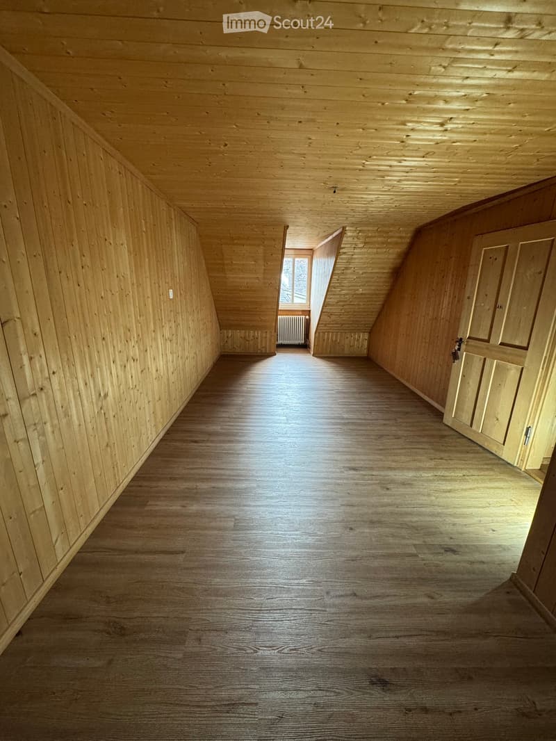 Empty wooden hallway with wooden walls, ceiling, and floor, featuring a window at the end and a closed door on the right side.