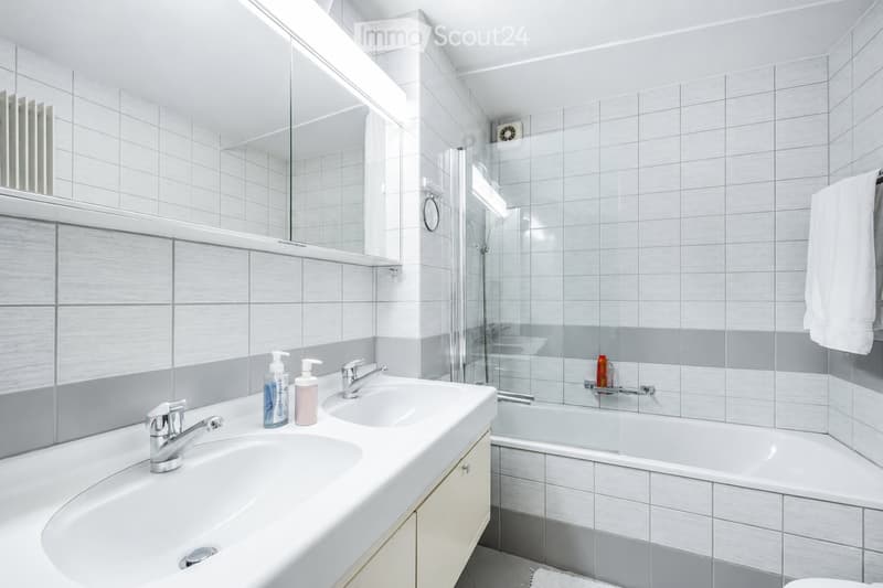 Modern bathroom with white tiled walls, a double sink, a bathtub, a large mirror, and a towel hanging on the side.