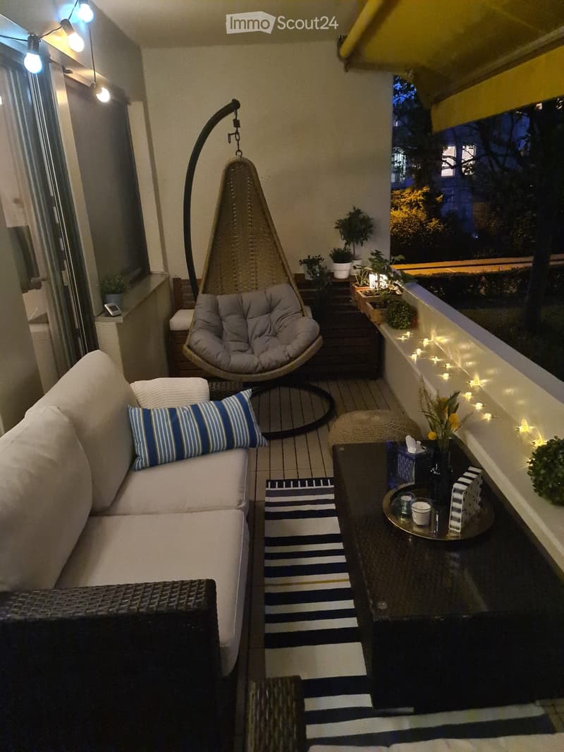 Balcony with a white sofa, blue and white striped cushions, a wicker hanging chair, a coffee table with drinks, and small potted plants.
