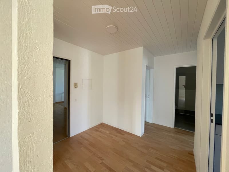 Empty hallway with wooden flooring, white walls, and several doors leading to other rooms.