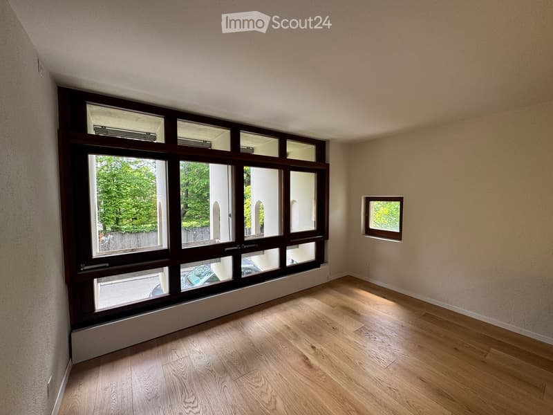 Empty room with wooden flooring, large windows, and light-colored walls.