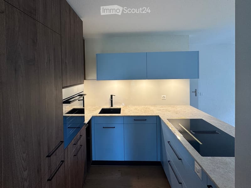 Modern kitchen with light blue cabinets, a central island with a sink and faucet, and a built-in stove on the right side.